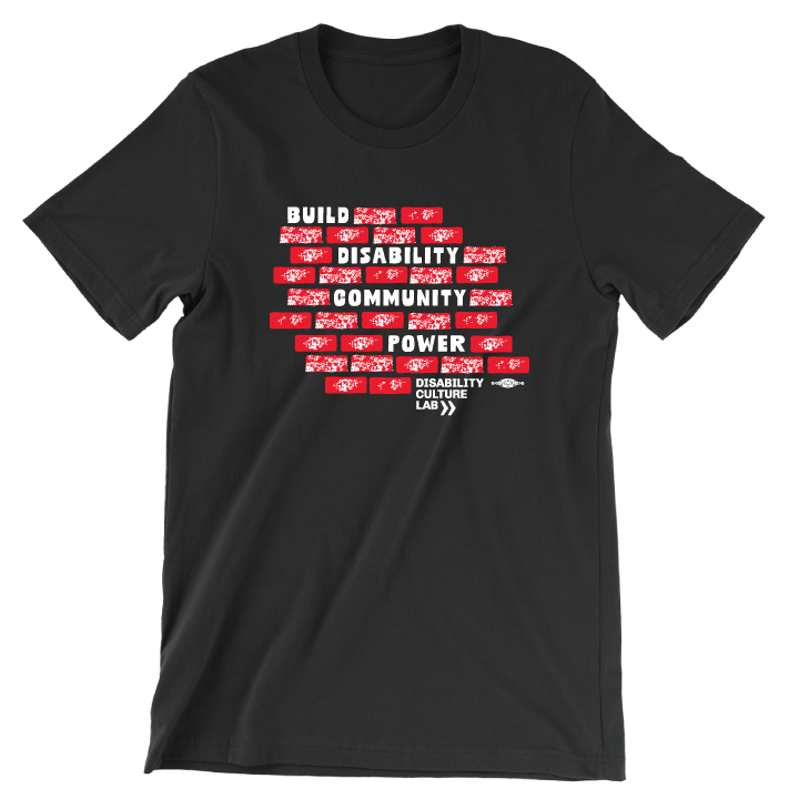 A black short sleeved T-shirt with a design of red bricks in the middle of the shirt. The bricks are surrounding bold white text that reads "Build Disability Community Power." Beneath the bricks is the white Disability Culture Lab logo with two white arrows.