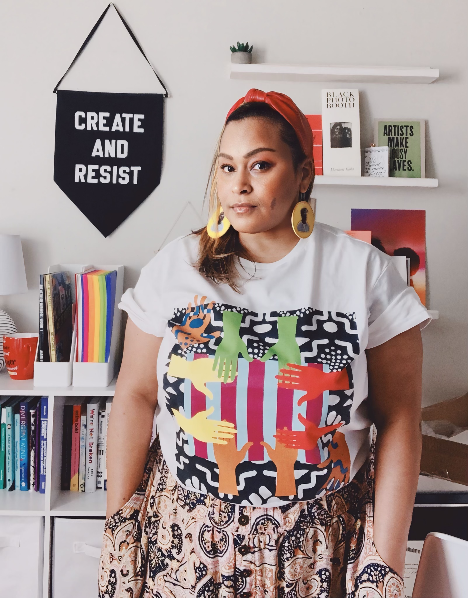 A bearded man in glasses and a T-shirt with "We Keep Us Safe" sits on a bed, smiling at a dog with a black and white coat. A small plant on a stool is in the background.