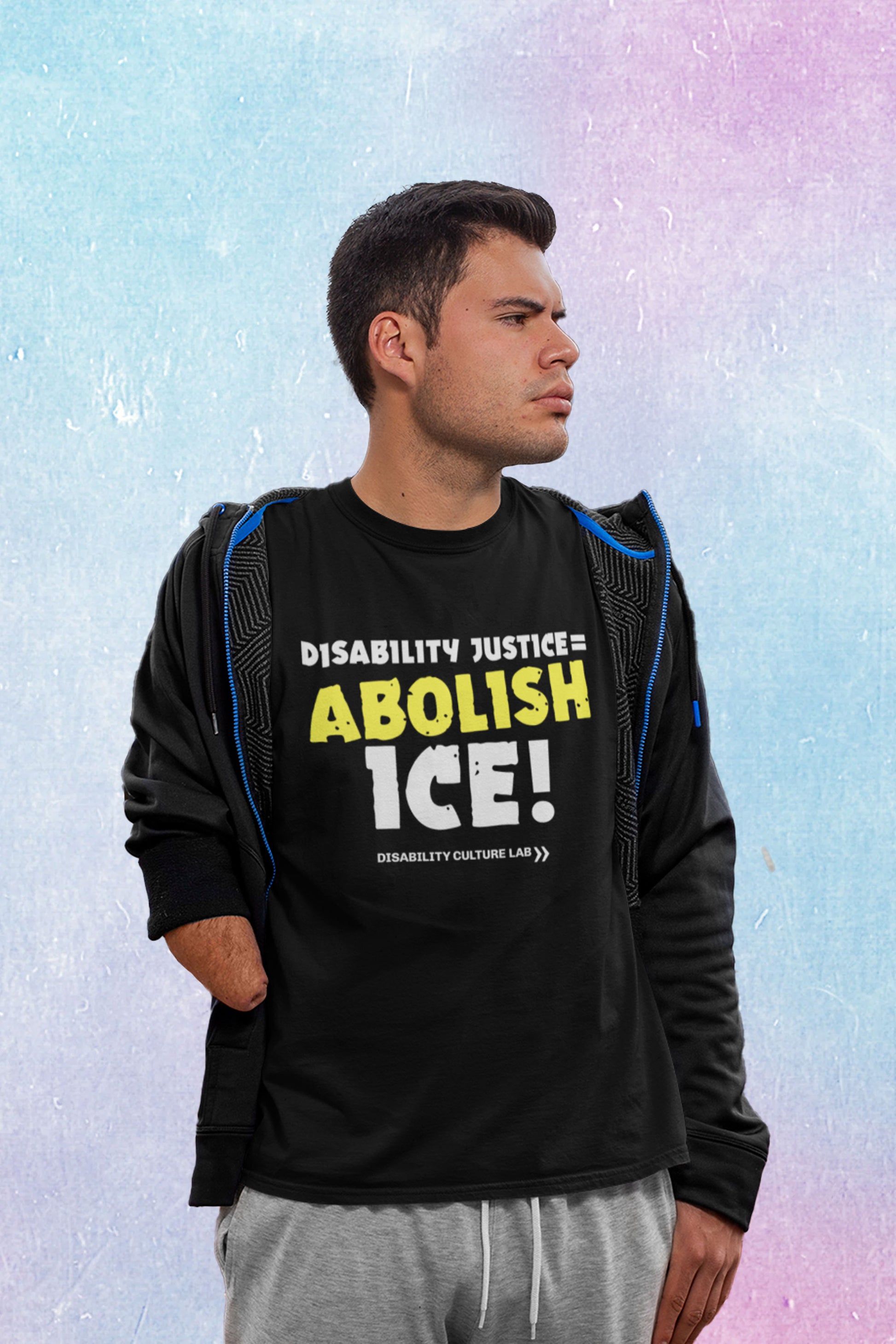 A brown-skinned person with short-cropped brown hair and limb difference looks off to the left. They are wearing a gray and blue jacket, gray sweatpants, and a black t-shirt that reads "Disability Justice = Abolish ICE!" in mostly white text, with "Abolish" in bright yellow and slightly tilted. Below is the white Disability Culture Lab logo.