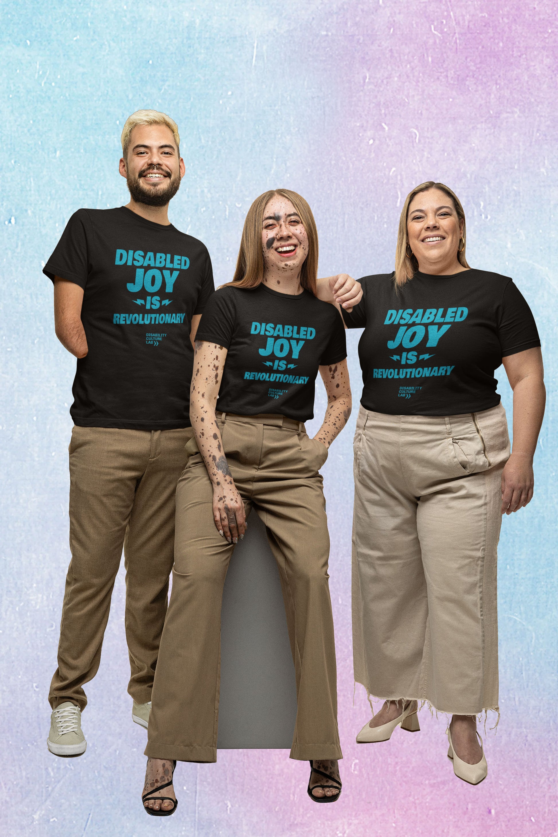 Three people wearing khaki pants and black t-shirts with the words "Disabled Joy Is Revolutionary" in turquoise and the Disability Culture Lab logo in turquoise smile brightly at the camera. 