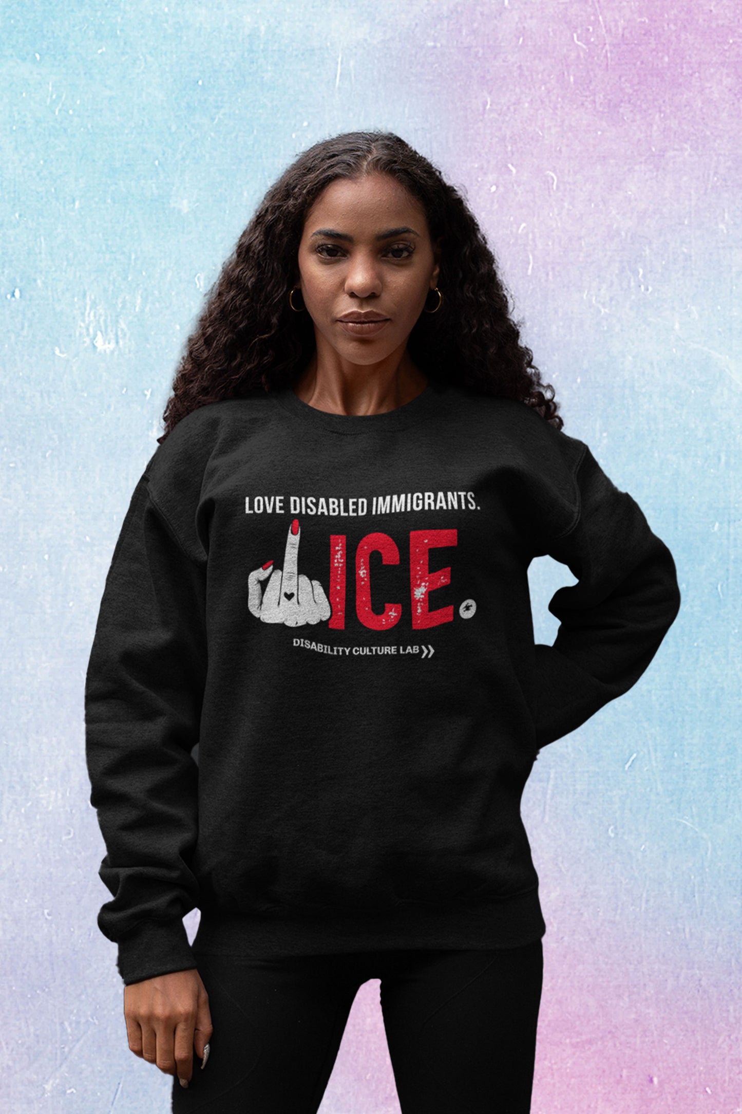 A Black person with long wavy hair poses standing, looking at the camera. They are wearing black leggings, and a black crewneck sweater that reads "Love Disabled Immigrants" in white text. Below is a hand with red nails and a black heart on the middle finger flipping the middle finger, and large textured text that reads "ICE," with "ICE" in red and the period in white. All together, the message can be read as "Love Disabled Immigrants. Fuck ICE." Below is the white Disability Culture Lab logo.