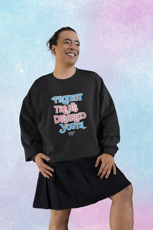 A gorgeous trans femme person in a black skirt and a black crewneck sweater that reads “Protect Trans Disabled Youth” in hand drawn letters in the trans pride flag colors (light pink, sky blue, and white). Below is the white Disability Culture Lab logo.