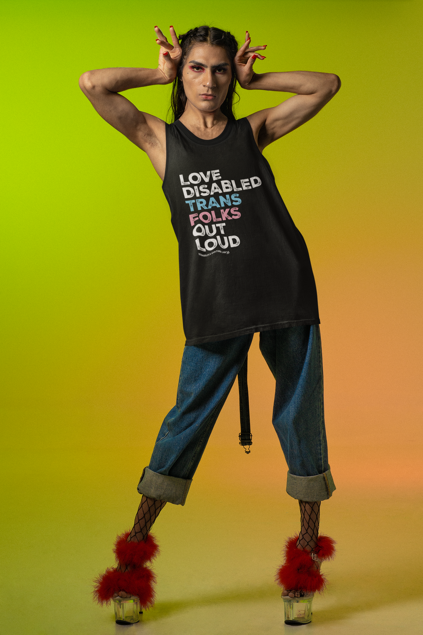 A person with light brown skin and long black hair. They have their hands up on either side of their head and are wearing blue jeans and a black muscle tank that reads, "Love Disabled Trans Folks Out Loud." The text is in the colors of the trans flag, with "Love Disabled" in white, "Trans" in light blue, "Folks" in light pink, and "Out Loud" in white. Below the design is the white Disability Culture Lab logo. They are also wearing read fuzzy high heels.