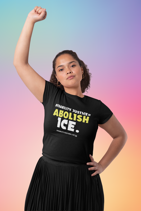 A person with light brown skin and long hair that is pulled back. They have their right fist in the air and are wearing a long black skirt and a black t-shirt that reads "Disability Justice = Abolish ICE." in mostly white text, with "Abolish" in bright yellow and slightly tilted. Below is the white Disability Culture Lab logo.