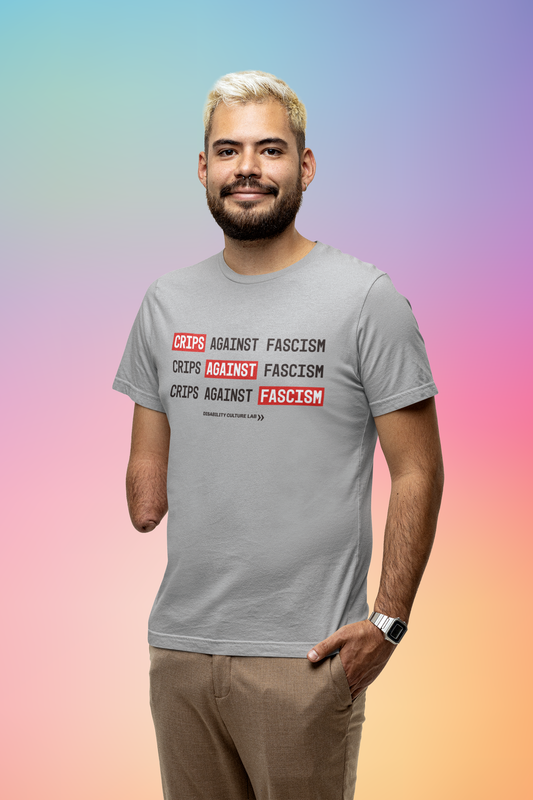 A person with light brown skin, short blonde hair, a beard, and a limb difference. They are wearing khakis and a gray t-shirt that reads, "Crips Against Fascism" three times, with "Crips" in the first line, "Against" in the second line, and "Fascism" in the third line all in white text with bright red background, so it also reads "Crips Against Fascism" diagonally. Below is the black Disability Culture Lab logo.