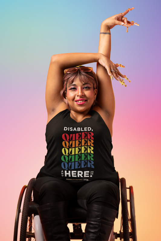 A person with light brown skin sits in a wheelchair, their hands above their head. They're wearing black pants, boots, and a muscle tank that reads, "Disabled, Queer, and Here 2026." "Disabled" is in black, and then "Queer" is written five times in a rainbow of colors, with a curve to the letters. Below that is black text that says "And Here." The "And" is written in small text vertically next to the "Here" which is the same size as "Disabled" and "Queer." To the right of that is "2026" in small text.