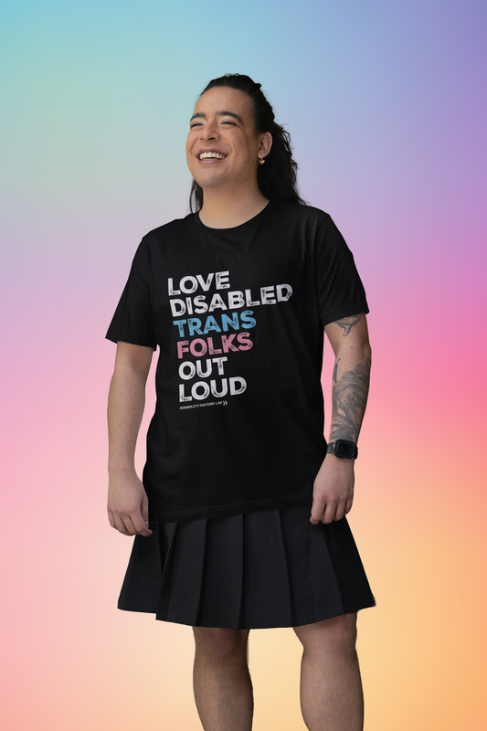 A person with light brown skin and dark hair that is pulled back. They are wearing a black skirt and a black short sleeve T-shirt that reads, "Love Disabled Trans Folks Out Loud." The text is in the colors of the trans flag, with "Love Disabled" in white, "Trans" in light blue, "Folks" in light pink, and "Out Loud" in white. Below the design is the white Disability Culture Lab logo.