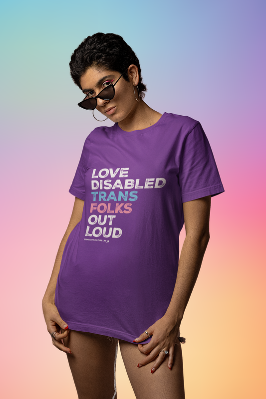 A person with brown skin and short dark hair. They are wearing sunglasses and a purple short sleeve T-shirt that reads, "Love Disabled Trans Folks Out Loud." The text is in the colors of the trans flag, with "Love Disabled" in white, "Trans" in light blue, "Folks" in light pink, and "Out Loud" in white. Below the design is the white Disability Culture Lab logo.