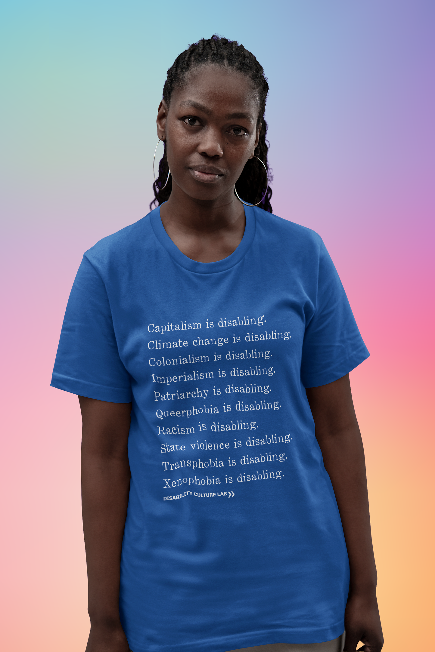A Black person with long braids that are tied back in a ponytail. They are wearing a royal blue short sleeve T-shirt with white serif text in a list reading, "Capitalism is disabling. Climate change is disabling. Colonialism is disabling. Imperialism is disabling. Patriarchy is disabling. Queerphobia is disabling. Racism is disabling. State violence is disabling. Transphobia is disabling. Xenophobia is disabling." Below the design is the white Disability Culture Lab logo.