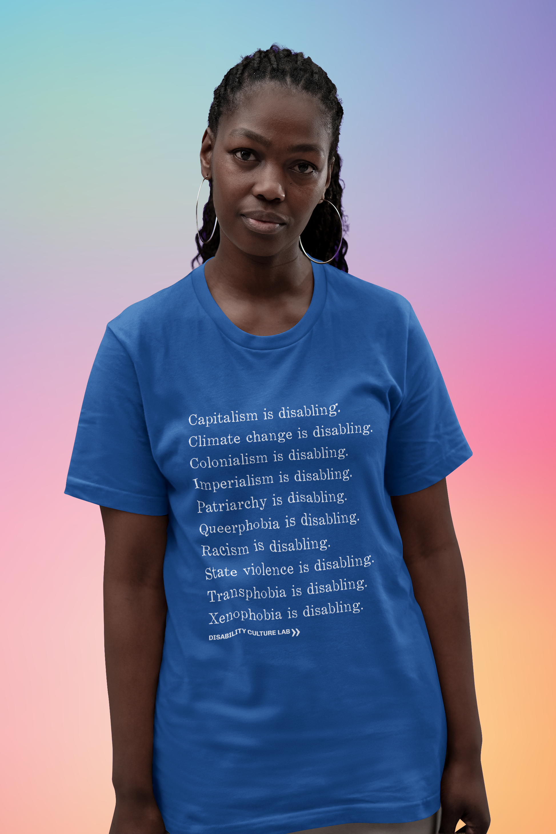 A Black person with long braids that are tied back in a ponytail. They are wearing a royal blue short sleeve T-shirt with white serif text in a list reading, "Capitalism is disabling. Climate change is disabling. Colonialism is disabling. Imperialism is disabling. Patriarchy is disabling. Queerphobia is disabling. Racism is disabling. State violence is disabling. Transphobia is disabling. Xenophobia is disabling." Below the design is the white Disability Culture Lab logo.