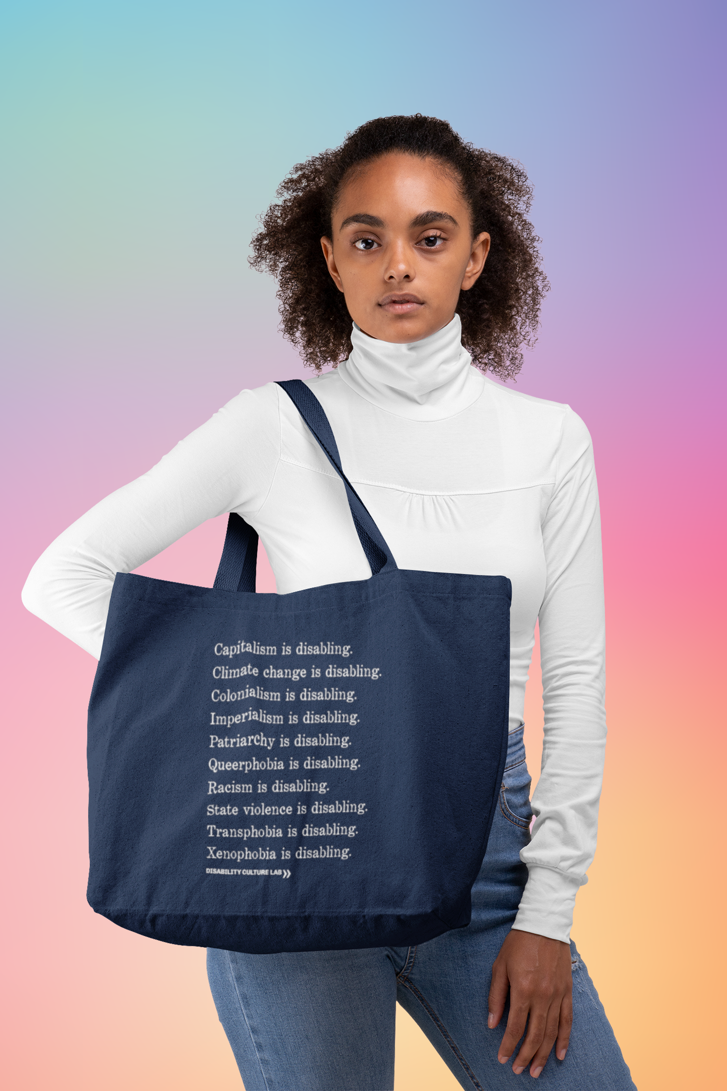 A Black person with long curly hair wearing a white long sleeve turtleneck and blue jeans. They are holding a navy blue tote bag with white serif text in a list reading, "Capitalism is disabling. Climate change is disabling. Colonialism is disabling. Imperialism is disabling. Patriarchy is disabling. Queerphobia is disabling. Racism is disabling. State violence is disabling. Transphobia is disabling. Xenophobia is disabling." Below the design is the white Disability Culture Lab logo.