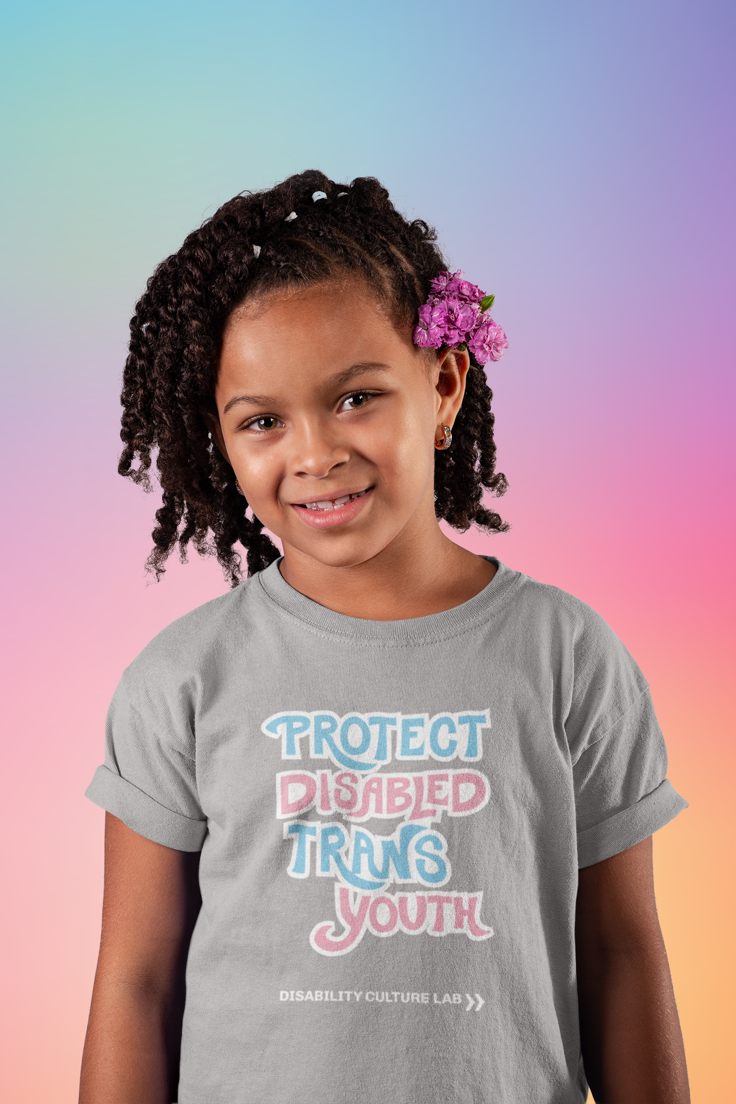 A very cute Black child with shoulder length twists and a flower in their hair wears a gray short sleeve T-shirt that reads “Protect Disabled Trans Youth” in hand drawn letters in the trans pride flag colors (light pink, sky blue, and white). Below is the white Disability Culture Lab logo.