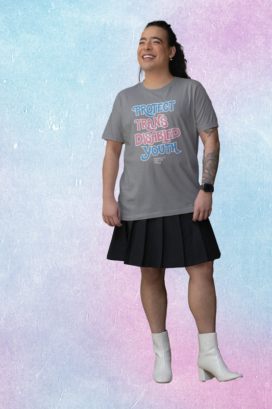 A gorgeous trans femme person in a grey t-shirt that reads “Protect Trans Disabled Youth” in hand drawn letters in the trans pride flag colors (light pink, sky blue, and white).