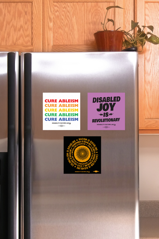 Three square magnets on the fridge. "Cure Ableism" in rainbow lettering for pride. "Disabled Joy is Revolutionary" in black letters on a purple background. "Oppression is Disabling" circular design in orange on a black background.