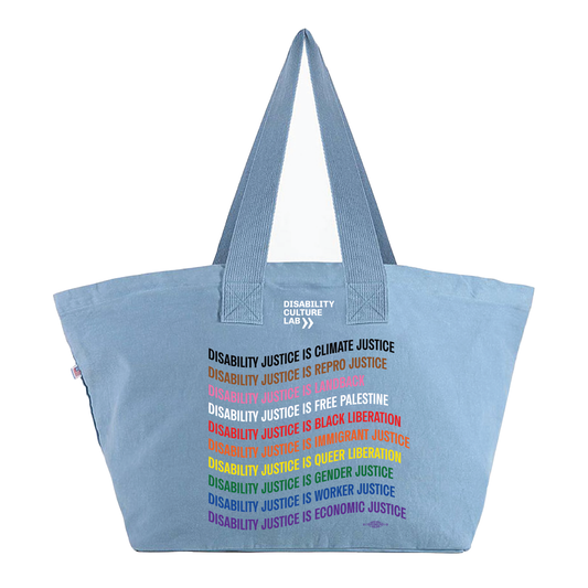 A picture of a denim bag with lettering line by line in rainbow Pride Flag colors. It reads: "Disability Justice Is... Climate Justice, Repro Justice, Landback, Free Palestine, Black Liberation, Immigrant Justice, Queer Liberation, Gender Justice, Worker Justice, Economic Justice." 